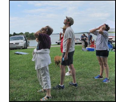 Picture shows 4 people standing and either holding or wearing eclipse sun shields over their eyes.